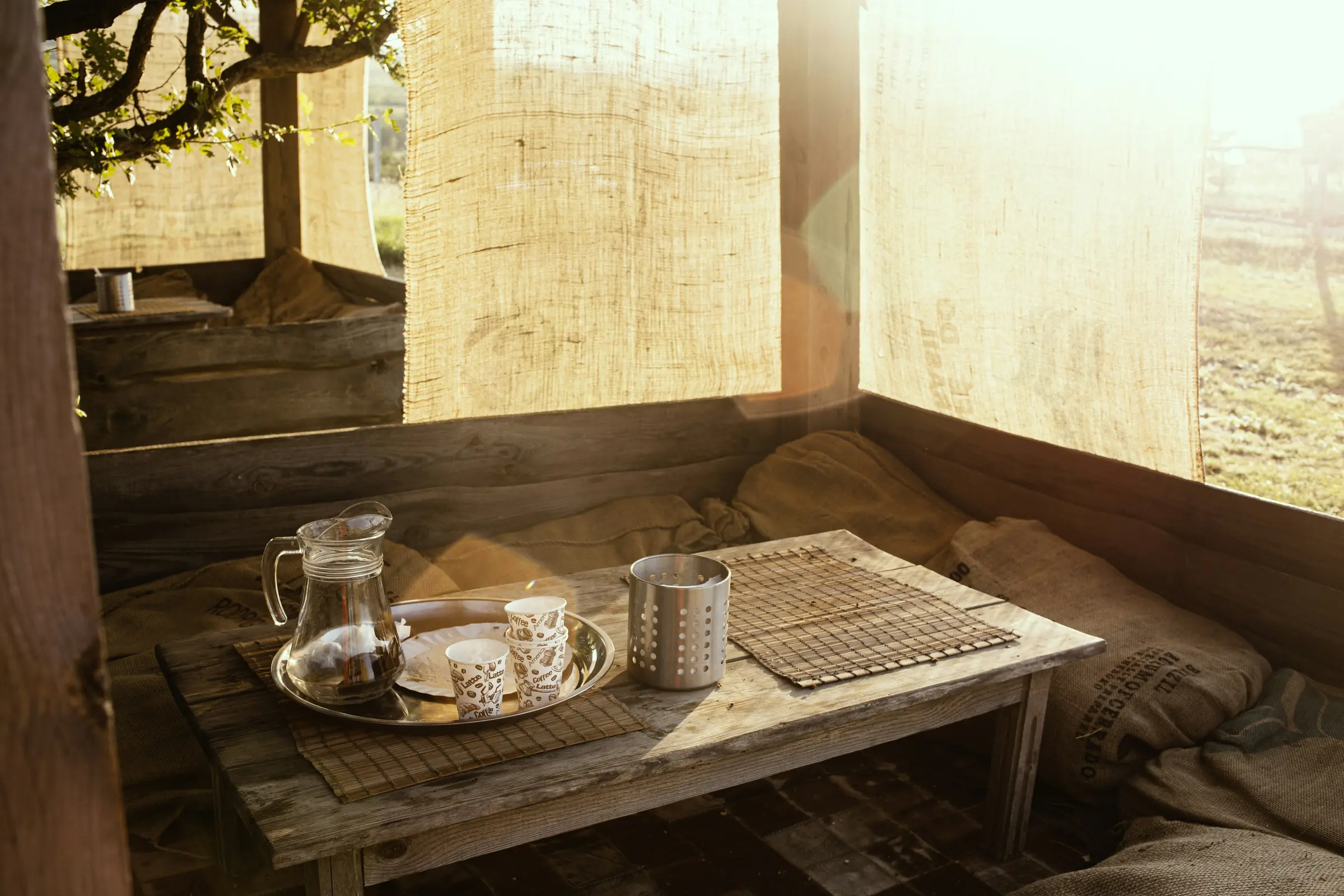 A low timber table set with a glass jug and two cups, morning light through a screen.