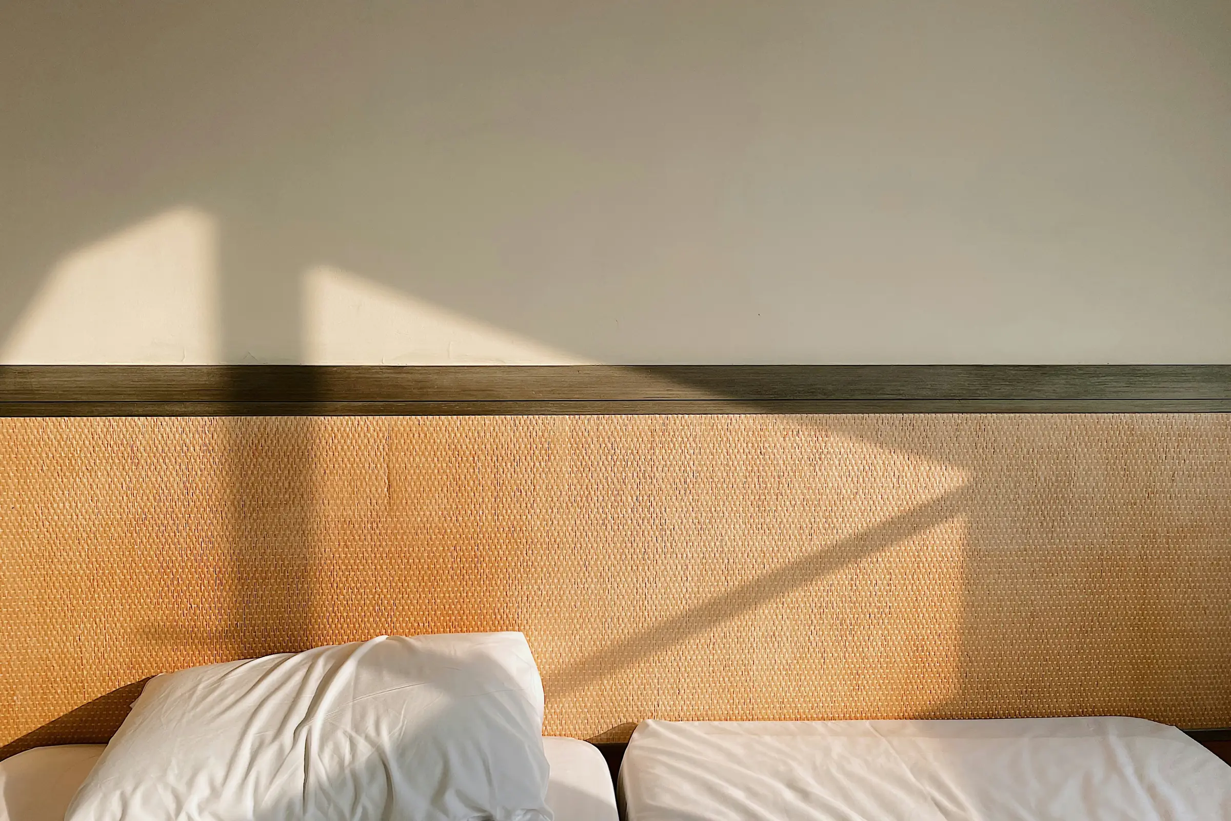 Late sun crossing a woven cane headboard and white pillows.