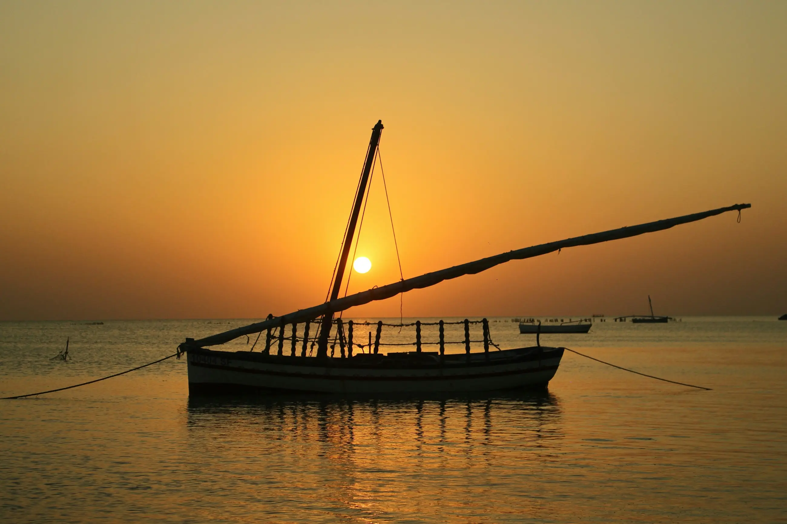 A wooden boat sitting still on flat water as the sun drops.
