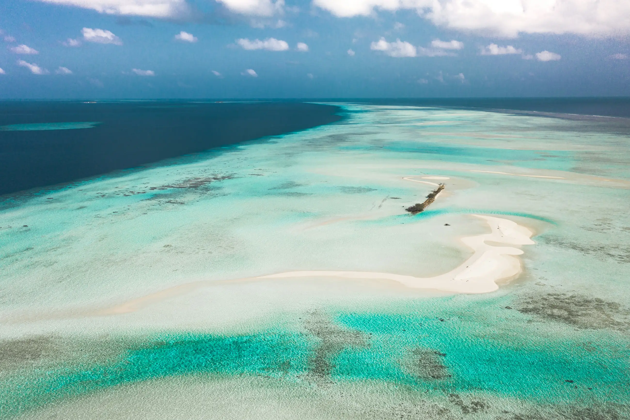 A bare spit of white sand curving out into turquoise water, seen from above.