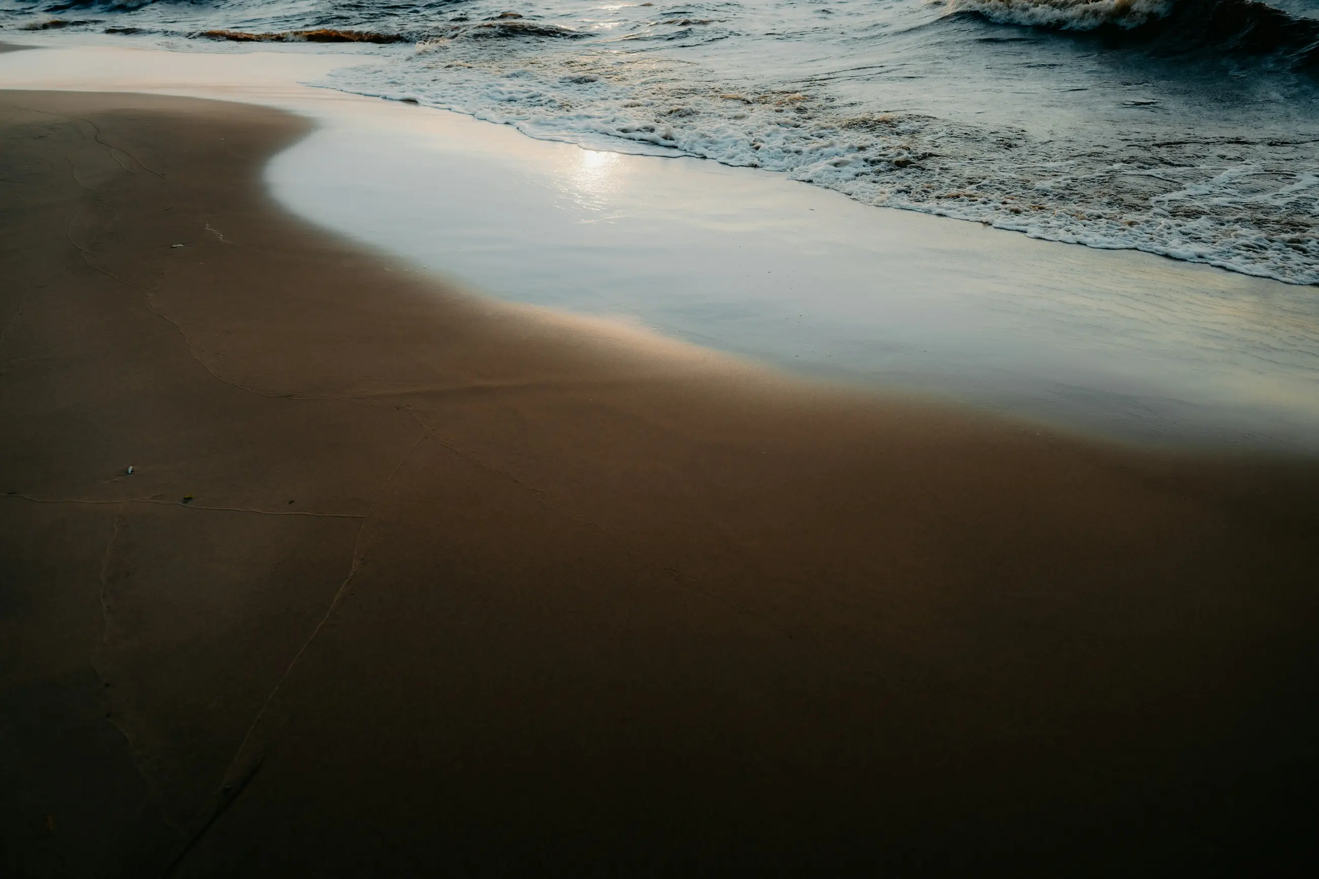 Low sun on wet sand where the water is running back off the beach.